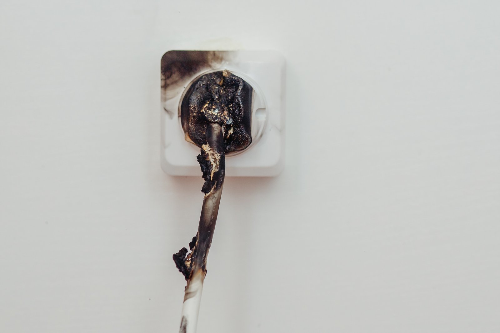 Close-up of a burnt electrical outlet with a melted and charred power cord, showing signs of electrical failure and fire hazard.