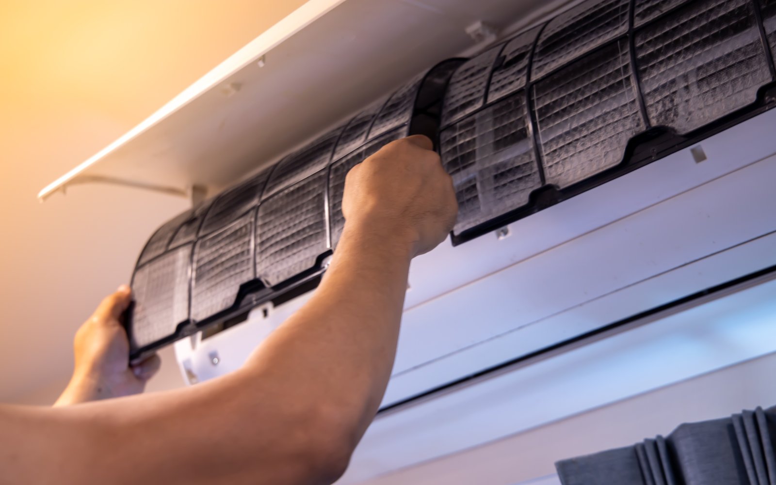 Person removing a dirty air conditioner filter from a wall-mounted unit for cleaning.