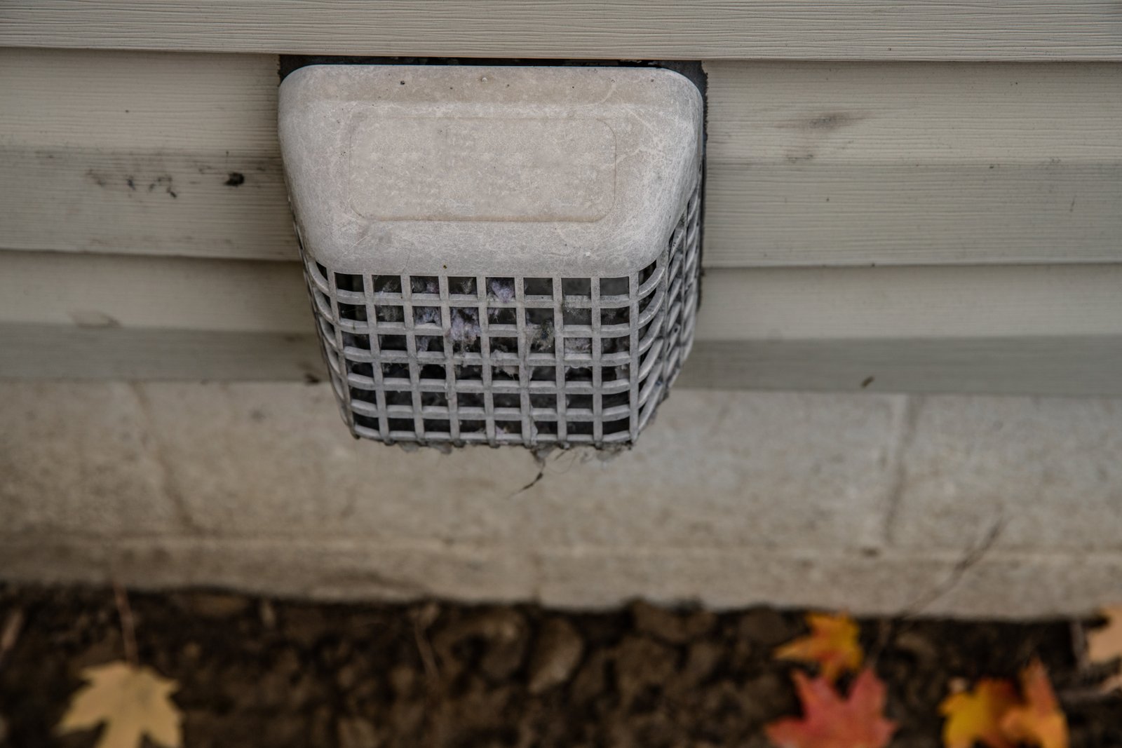 A clogged outdoor dryer vent cover with lint buildup, posing a potential fire hazard and reducing airflow efficiency.