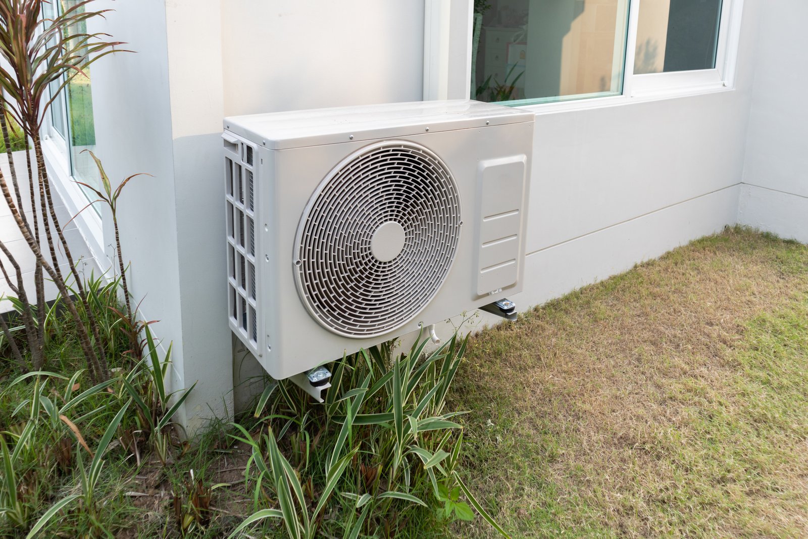 An exterior-mounted HVAC condensing unit attached to a residential building, positioned on a metal bracket above the ground.