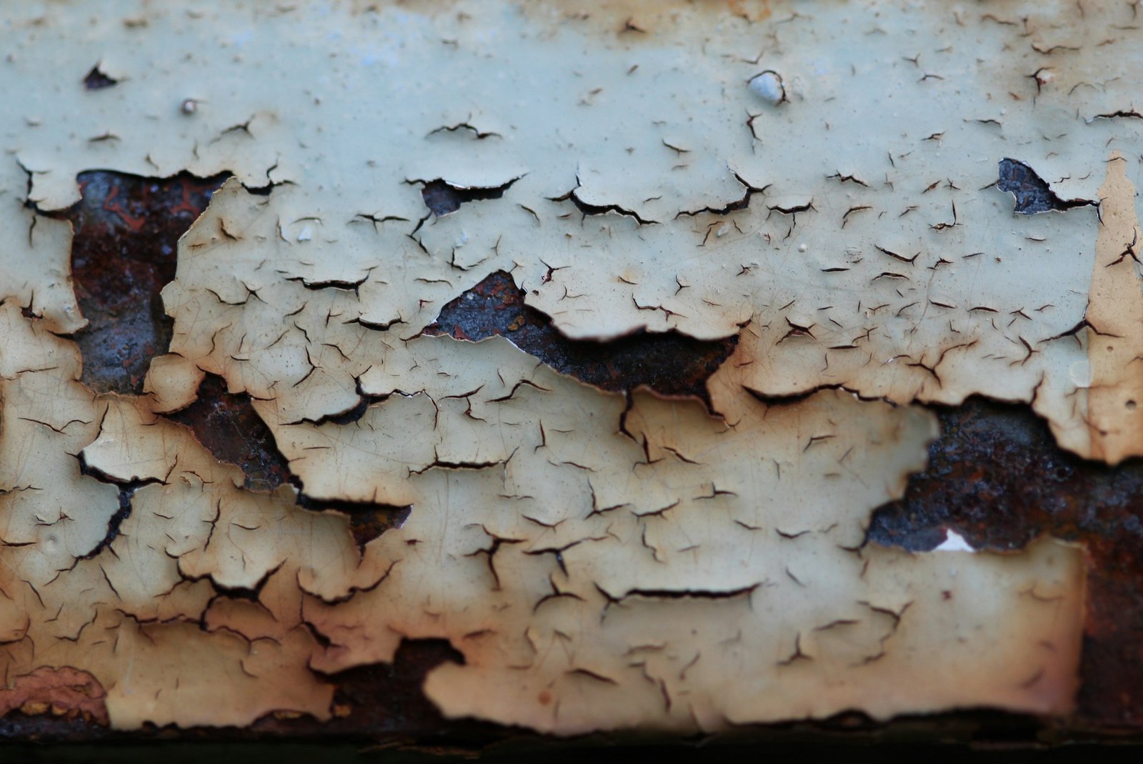Close-up of cracked and peeling beige paint revealing rusted metal underneath.