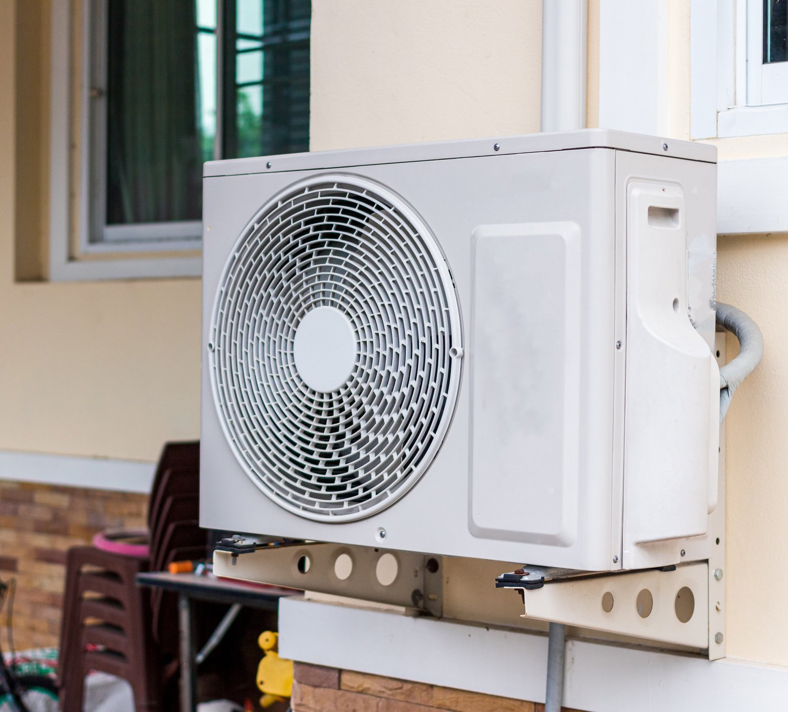A wall-mounted HVAC outdoor unit installed on a metal bracket outside a residential home, connected with insulated refrigerant lines.