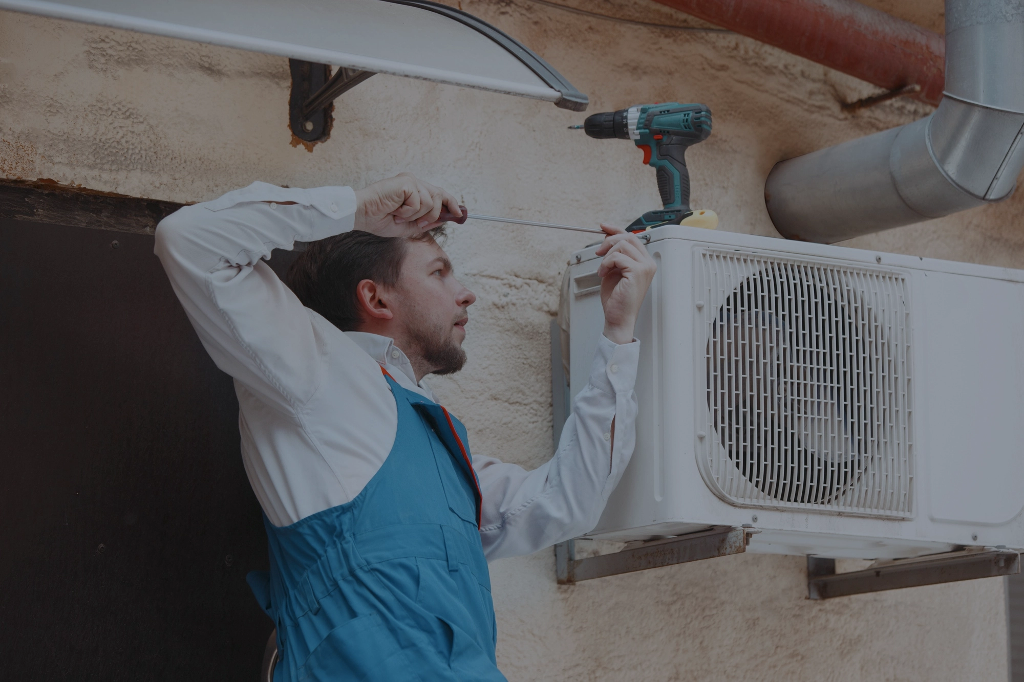 HVAC technician using a screwdriver to install an outdoor air conditioning unit on a building exterior